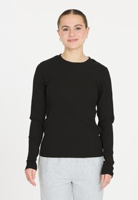 Schwarzes langärmliges Rippen-T-Shirt mit Rundhalsausschnitt und tailliertem Schnitt, kombiniert mit grauen Jogginghosen. Weiche Textur und nahtlose Bündchen.