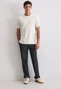 Hellgraues Baumwoll-T-Shirt mit Rundhalsausschnitt, kombiniert mit dunkelgrauer Hose und beigen Sneakern. Einfaches Design, lässige Passform.