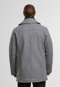 Grijze wollen jas met een gestructureerd ontwerp, voorzien van een brede kraag en lange mouwen. De stof heeft een gladde textuur met verborgen stiksels.