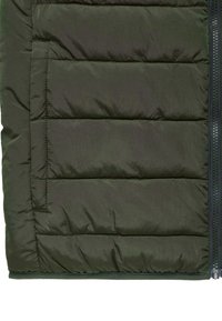 Vihreä pehmustettu takki, jossa on vaakasuora tikkaus, näkyvä vetskari oikealla ja sileä, kiiltävä pinta.