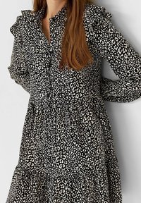 Vestido de estampado de leopardo en blanco y negro con cuello con volantes y mangas largas, que presenta un cierre frontal de botones y un detalle de cintura fruncida.