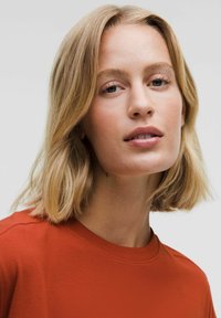 Īsām piedurknēm, ar apaļu kakla izgriezumu, krekls rūsas oranžā krāsā no kokvilnas. Gluda tekstūra ar brīvu piegriezumu un minimāliem šuvju detaļām.