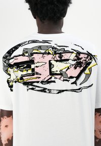 Hvit t-skjorte med et stort, abstrakt grafisk design i rosa, svart, grått og gult på baksiden, med en avslappet passform og mykt stoff.