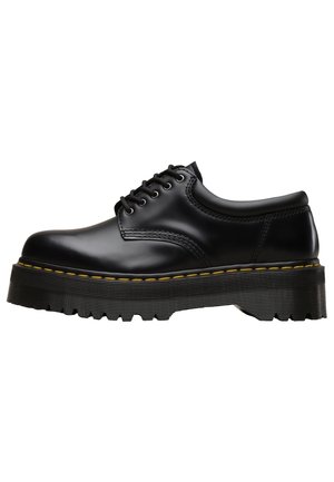 Black leather lace-up shoe with thick, ridged sole and yellow stitching along the sole edge, shown in side profile on a white background.