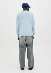 Light blue sweater with ribbed cuffs, paired with loose-fitting gray denim jeans. Black shoes complete the outfit.