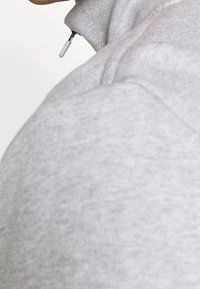 Grå sweatshirt med hög krage och dragkedja. Tyget verkar mjukt och strukturerat, med synliga sömnadsdetaljer.