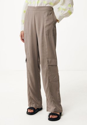 Taupe weite Hose mit seitlichen Cargotaschen, kombiniert mit schwarzen geflochtenen Sandalen und einer weißen Bluse mit gelben Mustern.