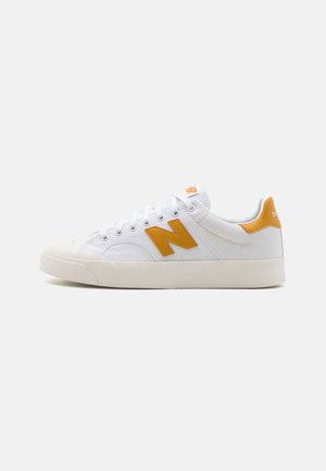 White low-top sneaker with orange accents, laces, and a thick sole, shown from the side on a plain background.