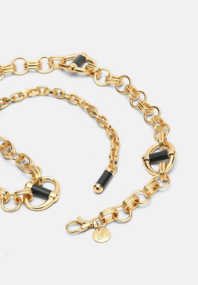 Cadena de oro con grandes eslabones ovalados, intercalados con acentos de caucho negro. Incluye un cierre con broche y una medalla con el logo desmontable.