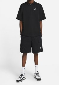 Zwarte Nike polo met korte mouwen, gecombineerd met bijpassende cargoshorts. Gekozen met witte Nike sokken en zwarte sneakers.