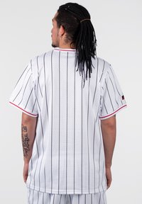 Hvid mesh-jersery med sorte lodrette striber, røde detaljer på kraven og ærmerne, korte ærmer og en loose fit. Bagfra ses der ingen logoer.