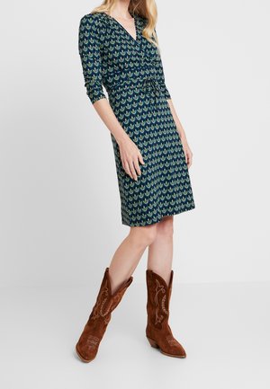 Granatowa sukienka w zielone liściaste wzory, dekolt w serek, rękawy o długości 3/4 oraz ściągnięta talia. Dobrana do brązowych zamszowych kowbojskich botków z detalami.