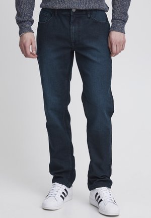 Mørkeblå denimjeans med klassisk rett passform, fem lommer og glidelås. Brukt med hvite sneakers med svarte striper.