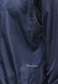 Μπλε ναυτικό μπουφάν με εσωτερική φόδρα με σχέδιο και τυπωμένο λογότυπο με το κείμενο "ONLY PLAY" στο ύφασμα.