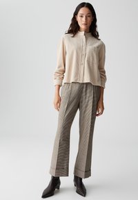 Beige geribde button-up shirt met een puntig kraag, gecombineerd met bruin geruit broek en zwarte enkelboots. Licht, textuurstof zichtbaar.