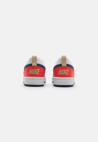 Nike sneakers featuring a combination of white, red, and navy materials. Back displays large gold "NIKE" logos and a tan heel tab.