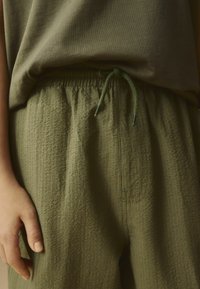 Pantalontexturé vert olive avec taille élastique et cordon de serrage. Design simple avec une coupe ample, associé à un haut assorti.
