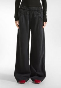 Pantaloni neri a gamba larga in denim, con cintura elastica, due tasche frontali e una texture liscia. I fondi sono leggermente svasati.