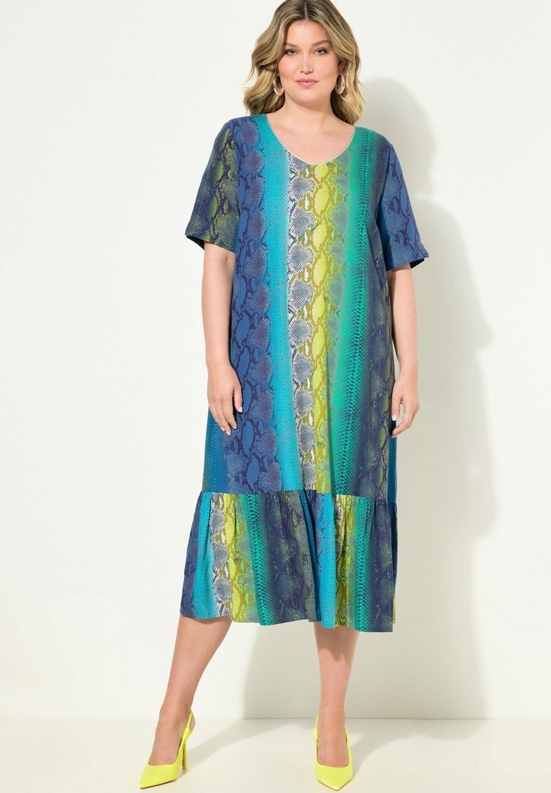 Maxi-Kleid mit Schlangenprint in Blau-, Grün- und Türkistönen, mit gestuftem Saum, kurzen Ärmeln und V-Ausschnitt. Kombiniert mit gelben Absatzschuhen.