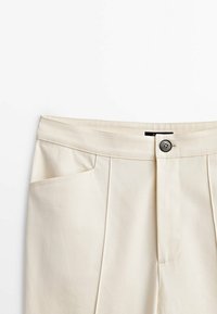 Pantalon beige à la texture lisse, avec une fermeture à un seul bouton, des poches latérales, et des plis avant bien repassés.