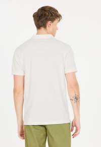 Vit kort�ärmad polo med krage, med en enkel design. Tillverkad av bomull med rak nederkant; synlig tatuering på höger arm.