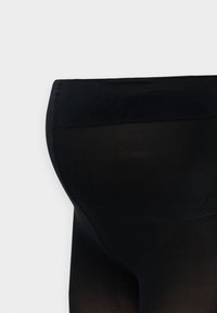 Μαύροι ημιδιαφανείς καλσόν εμφανιζόμενοι από τη λεκάνη έως το μέσο του μηρού πάνω σε απλό φωτεινό φόντο.