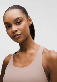 Helles rosa Sportoberteil mit rundem Ausschnitt und breiten Schulterträgern. Glatte Textur, taillierte Passform betont die Schultern und das Schlüsselbein.