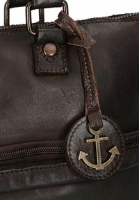 Borsa a tracolla in pelle marrone con zip, accessori metallici e un'etichetta ad ancoraggio circolare. Texture sottile con dettagli di cucitura a contrasto.
