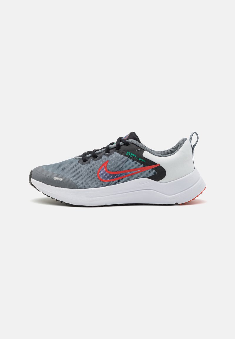 Baskets de sport grises avec une tige en mesh, des lacets noirs, un logo swoosh rouge et une semelle blanche avec des accents rouges. Présence d'une languette au niveau du talon.