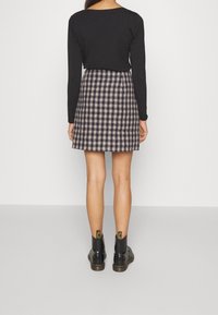 Top negro de manga larga combinado con una falda de patinadora a cuadros en tonos azul marino y beige, complementado con botas negras hasta el tobillo con acentos amarillos.