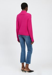 Fuchsia Strickpullover mit hohem Kragen, gerippten Bündchen und Saum, kombiniert mit blauen cropped Jeans und schwarzen Schlupfheels.