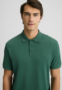 Polo shirt verde scuro realizzato in tessuto morbido, con colletto, patta con tre bottoni e logo discreto sul petto sinistro.