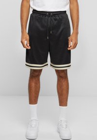 Svart idrettsshorts med mesh-struktur, hvite striper ved kanten og snøring i livet. Stilfullt kombinert med hvite joggesko og sokker.