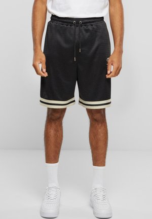 Pantaloni scurți sport negri, cu textură din plasă, accente albe la margine și talie cu șnur. Stilizați cu adidași și șosete albe.