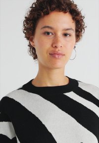 Maglione a righe nere e grigie, realizzato in tessuto a maglia, con colletto rotondo e motivo testurizzato visibile. Vestibilità casual, con una leggera lucentezza.