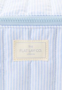 Blå og hvit stripet stoff med en lyseblå glidelås og en kremfarget etikett med "THE FLAT LAY CO. LONDON" i blå tekst.