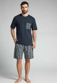 Camisa de manga corta azul marino con un bolsillo a cuadros, combinada con shorts de patrón a cuadros en azul marino, verde y blanco. Material suave de algodón.