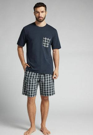 Navy-blaues kurzärmliges Hemd mit einer karierten Tasche, kombiniert mit karierter Shorts in Navy, Grün und Weiß. Hergestellt aus weicher Baumwolle.