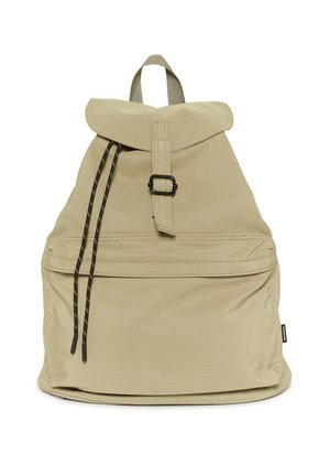 Beige kangaskuorinen reppu, jossa on etutasku vetoketjulla, musta solkindatu, mustat kiristysnauhat ja yläkädensija.