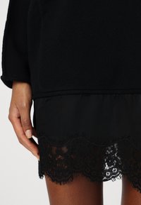 Abito nero con un top in maglia testurizzata e una gonna in tessuto nero a strati. I dettagli in pizzo all'orlo aggiungono un tocco decorativo.