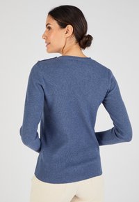 Pull bleu côtelé à manches longues, col rond et boutons aux épaules. Texture de tissu douce, coupe ajustée et ourlet légèrement arrondi.