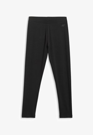 Jong persoon met een grijze hoodie, zwarte legging, witte sokken, zwart-witte sneakers, zwarte crossbody tas en een zwarte sjaal met patroon om de hals.