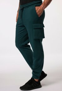 Teal Jogginghosen aus weichem Stoff mit elastischem Bund, seitlichen Taschen und einer Klappen-Cargotasche am Oberschenkel.