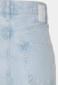 Jeans de denim azul claro com uma cintura de altura média, bolsos traseiros e um retângulo em couro branco na cintura. Tecido texturizado com acabamento lavado.