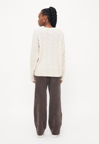 Krem pulover s pletenicom i opuštenim krojem, uparen s širokim smešnim hlačama od kordura. Mekana tekstura i vidljivi detalji šivanja.