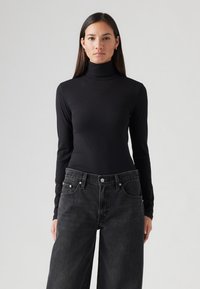 Top de cuello alto negro de manga larga, hecho de tela de canalé, con un diseño ajustado, combinado con jeans oscuros de pierna ancha y cintura alta.
