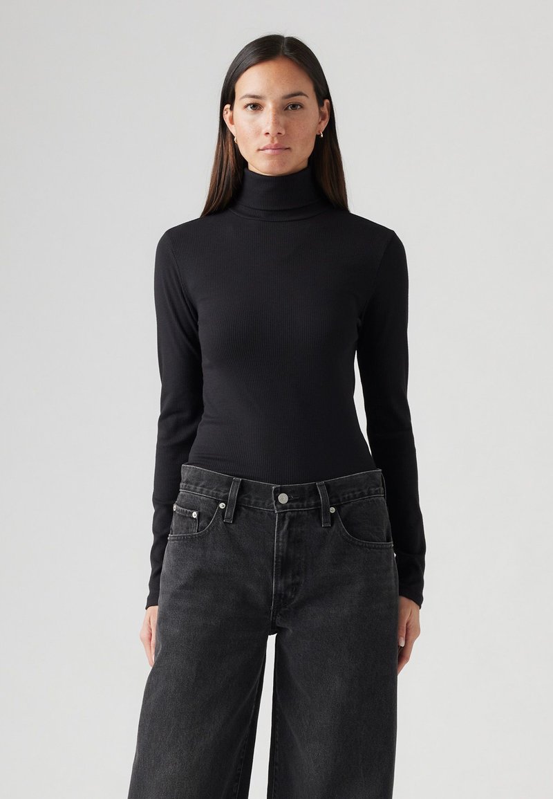 Haut à manches longues noir en col roulé, en tissu côtelé, au design ajusté, associé à un jean large taille haute gris foncé.