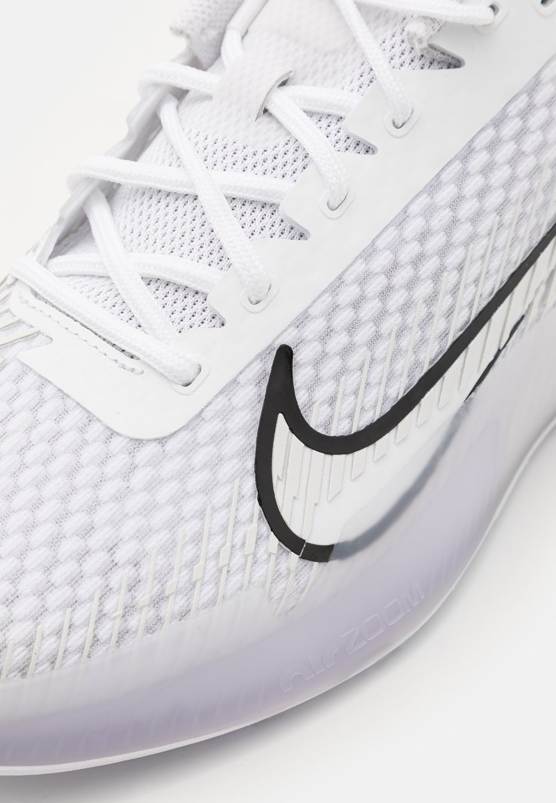 Zapatilla Nike blanca con parte superior de malla, logo Swoosh negro, acentos texturizados y una suela translúcida con el lema "Air Zoom".