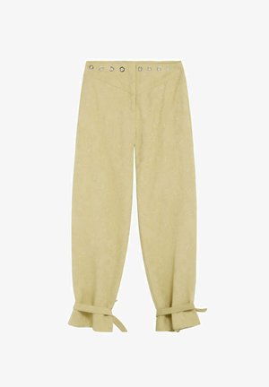 Pantalon beige clair à taille haute, œillets métalliques autour de la taille et volants noués aux chevilles.