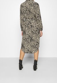 Dlouhé béžové šaty s černými zebřími pruhy, s dlouhými rukávy a vysokým výstřihem. V páru s černými kotníkovými botami.